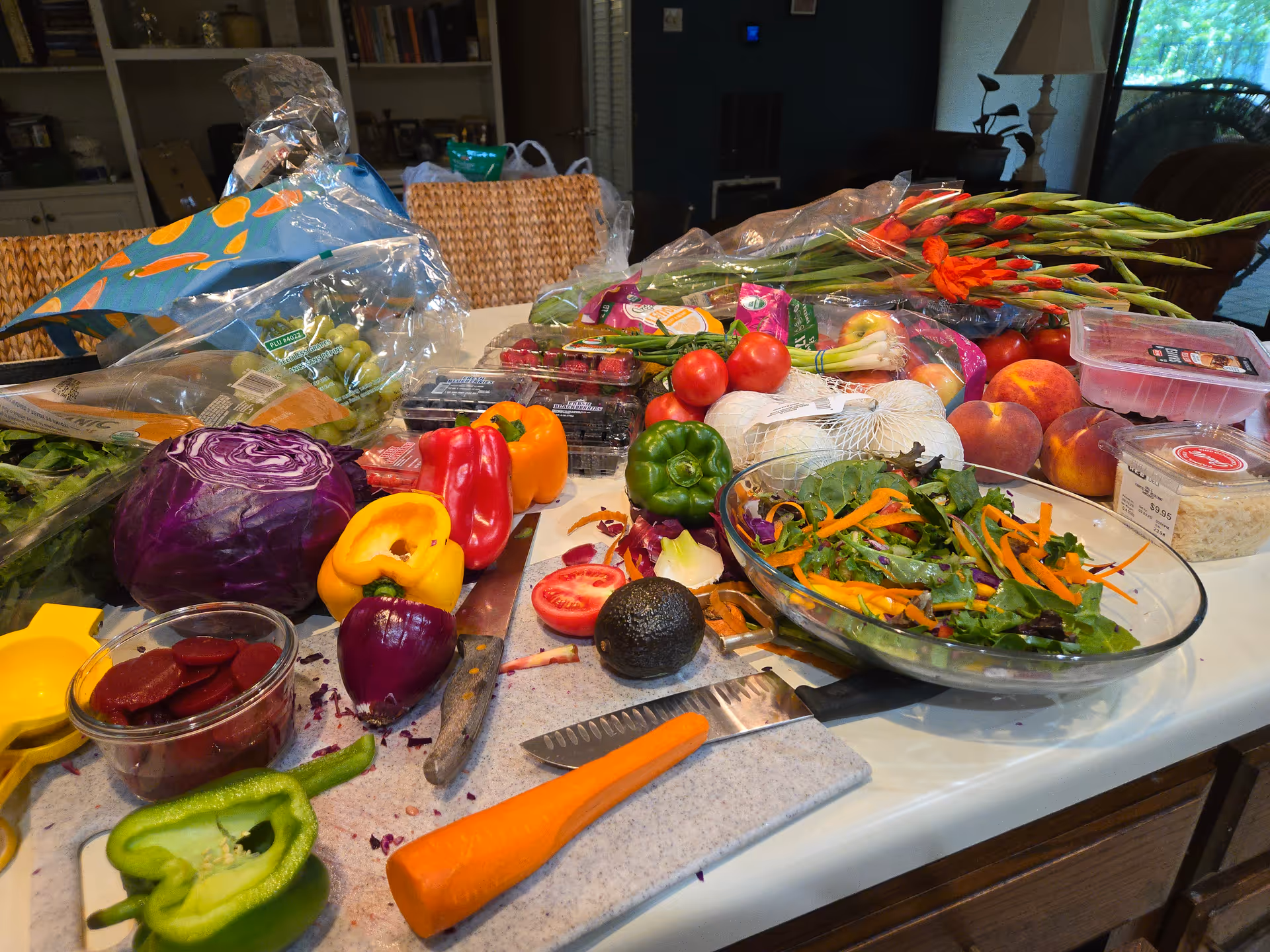 A cluttered kitchen counter with fresh vegetables, salad, and cooking tools.