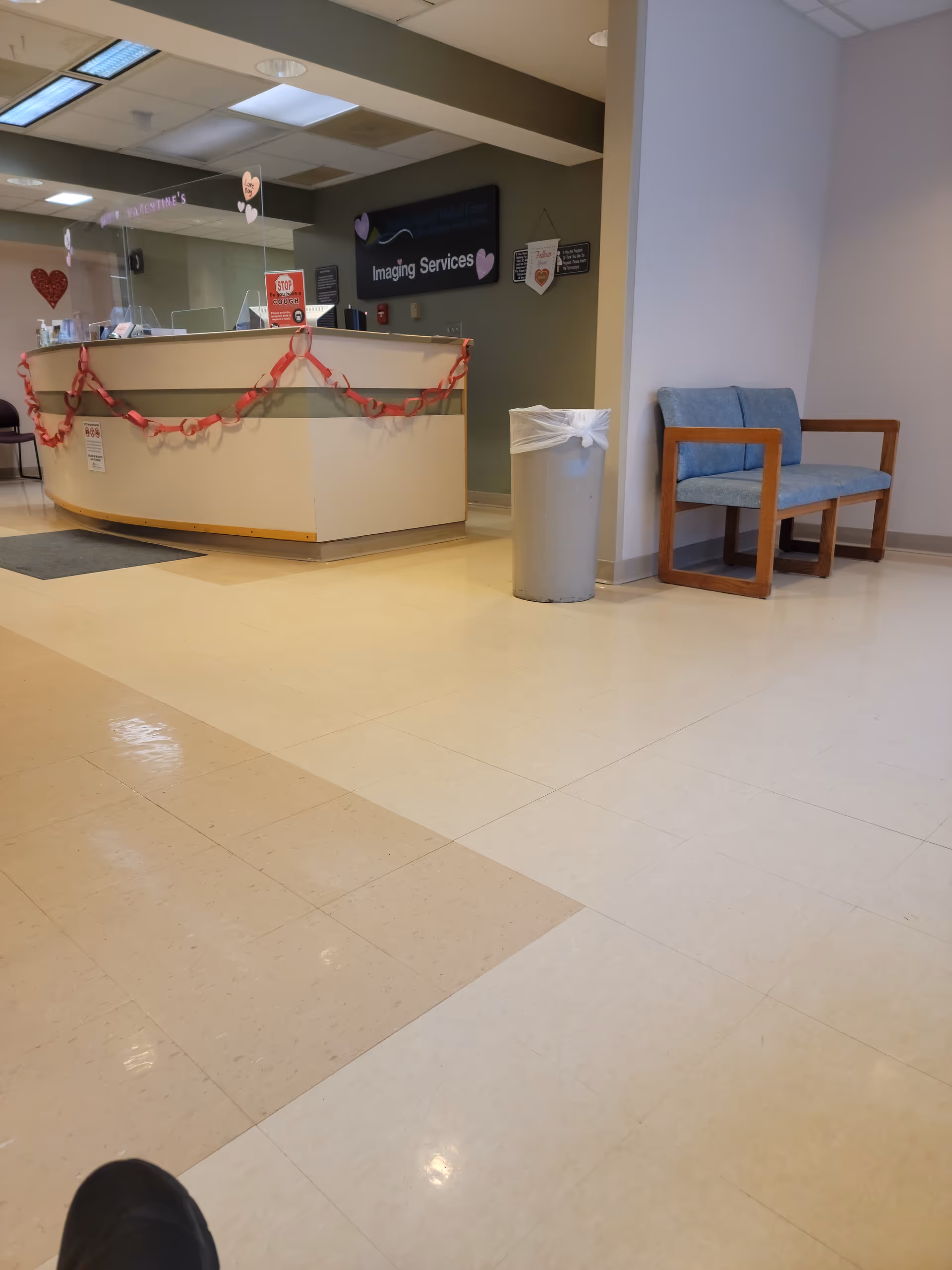 Hospital reception area with curved desk, Imaging Services sign, valentine decorations, trash can, and blue chairs.