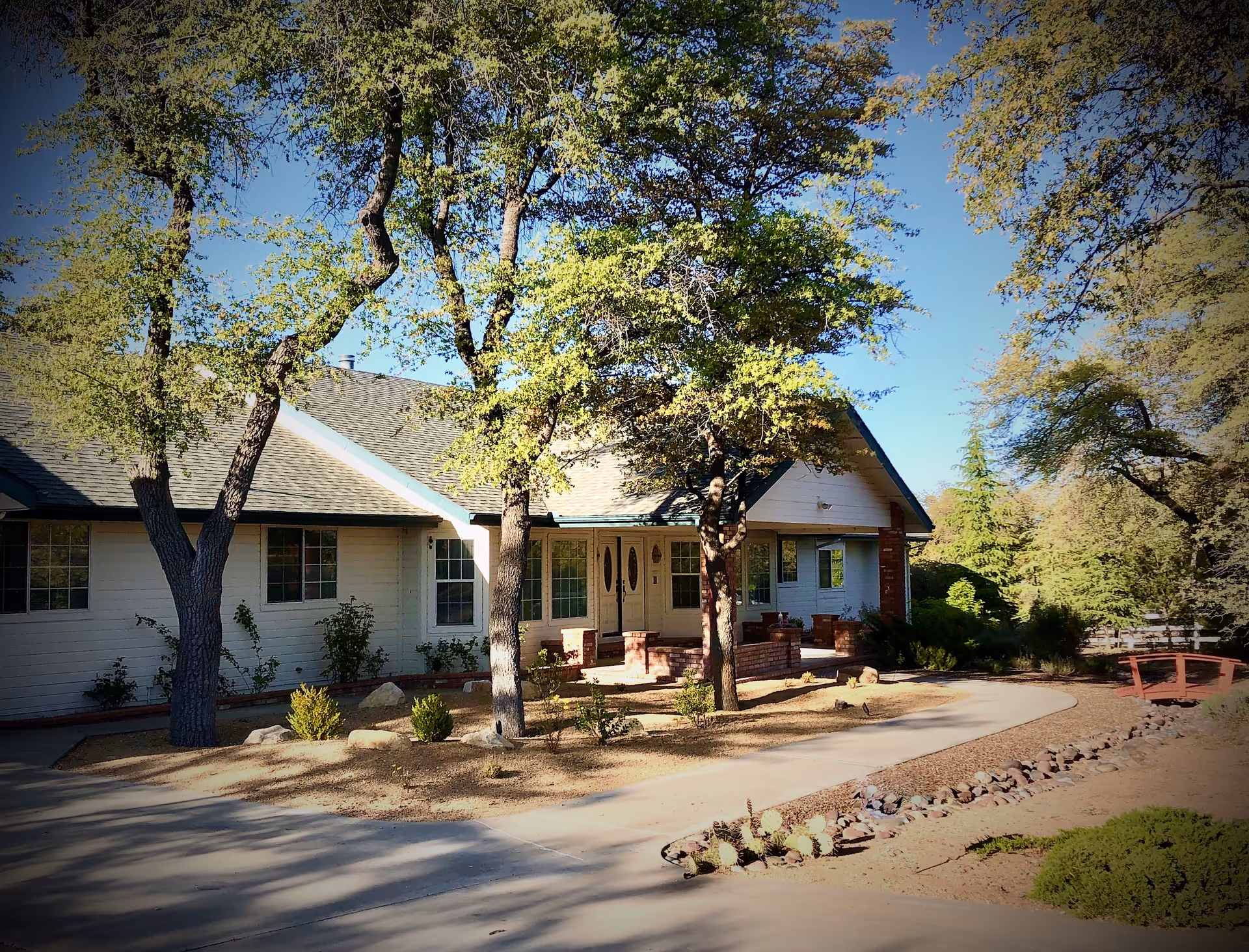 Single-story senior living building with front porch, landscaped path, and surrounding trees.