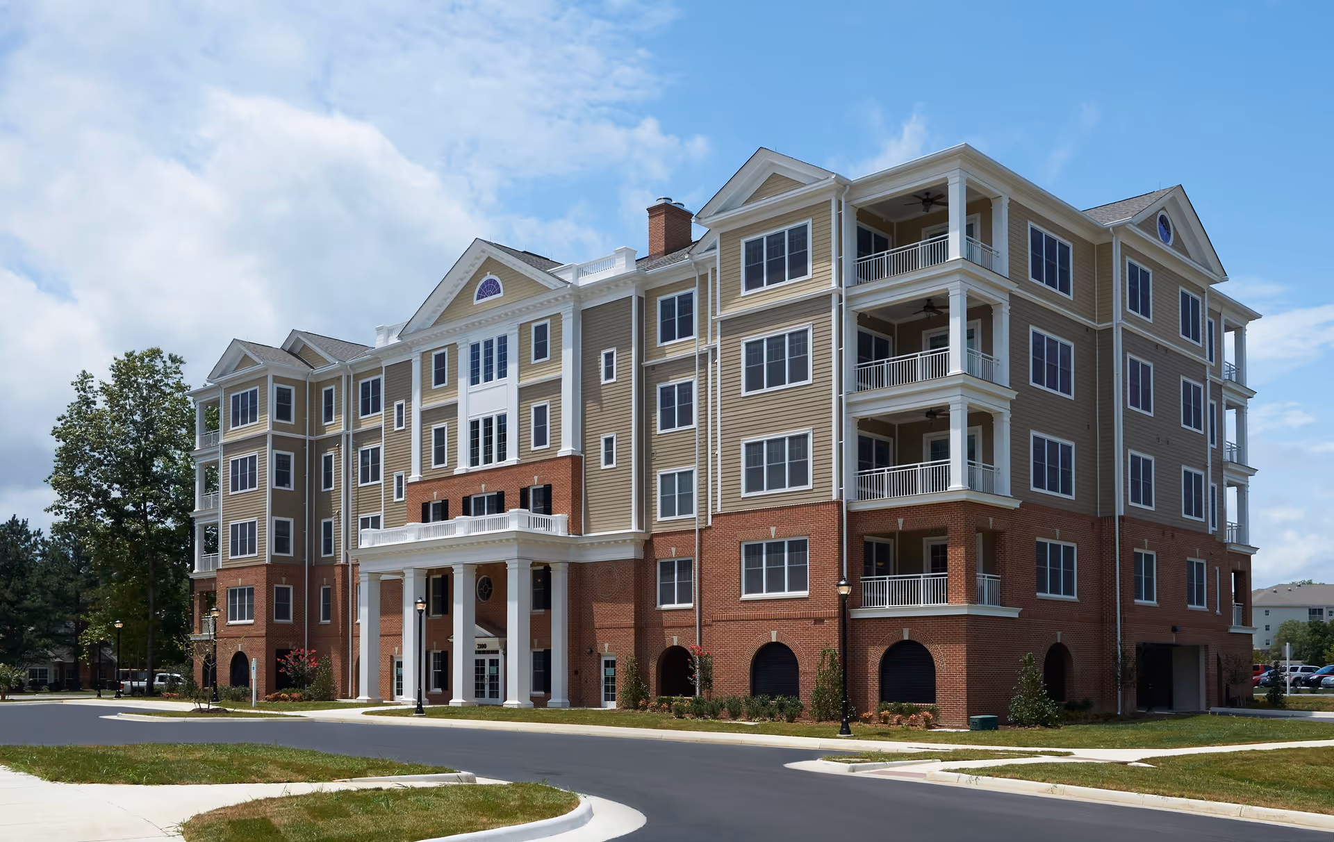 A multi-story senior living building with brick base, tan siding, and balconies.