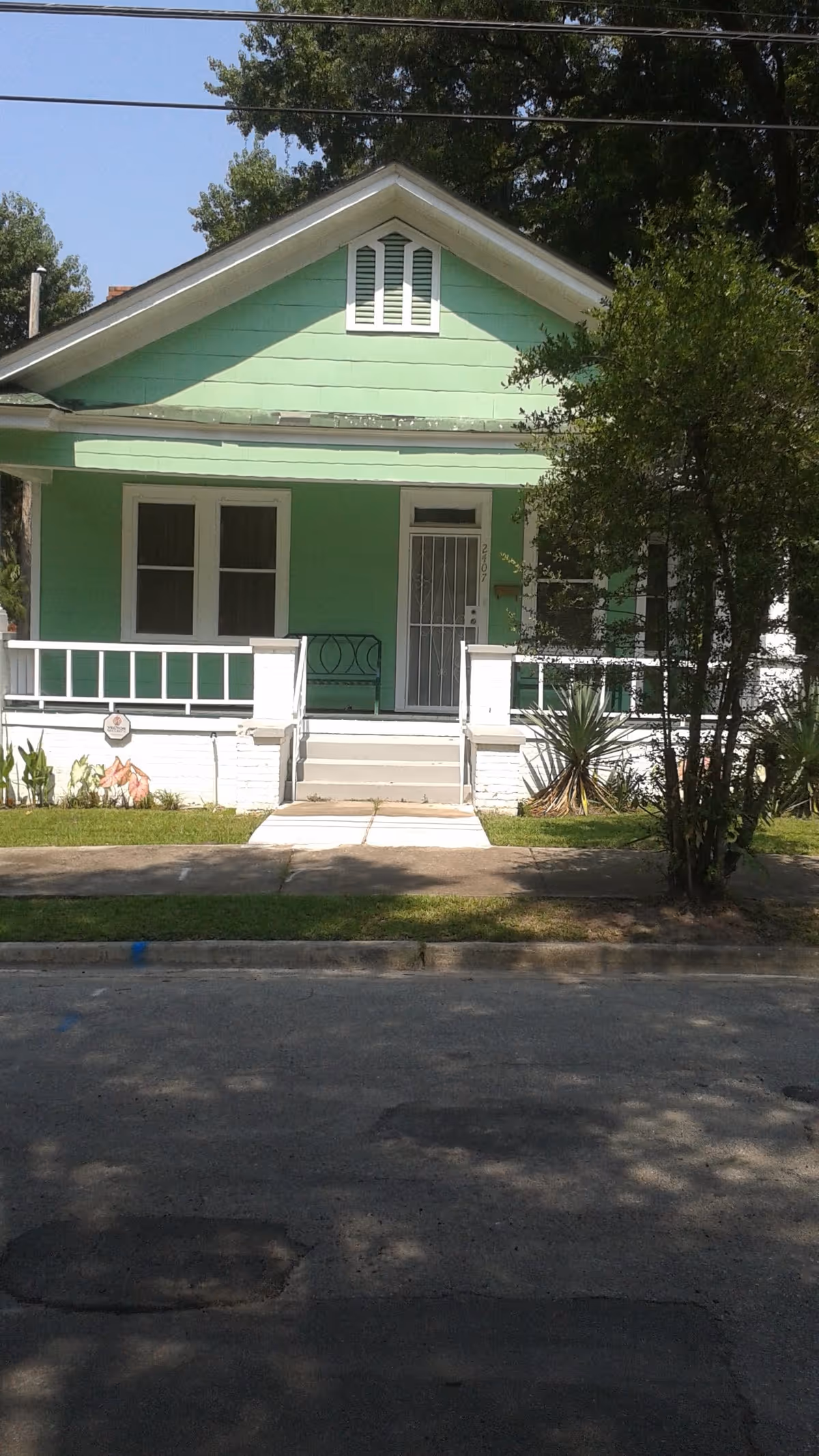 Front exterior of a small mint-green bungalow with a covered porch, steps, and a barred front door.