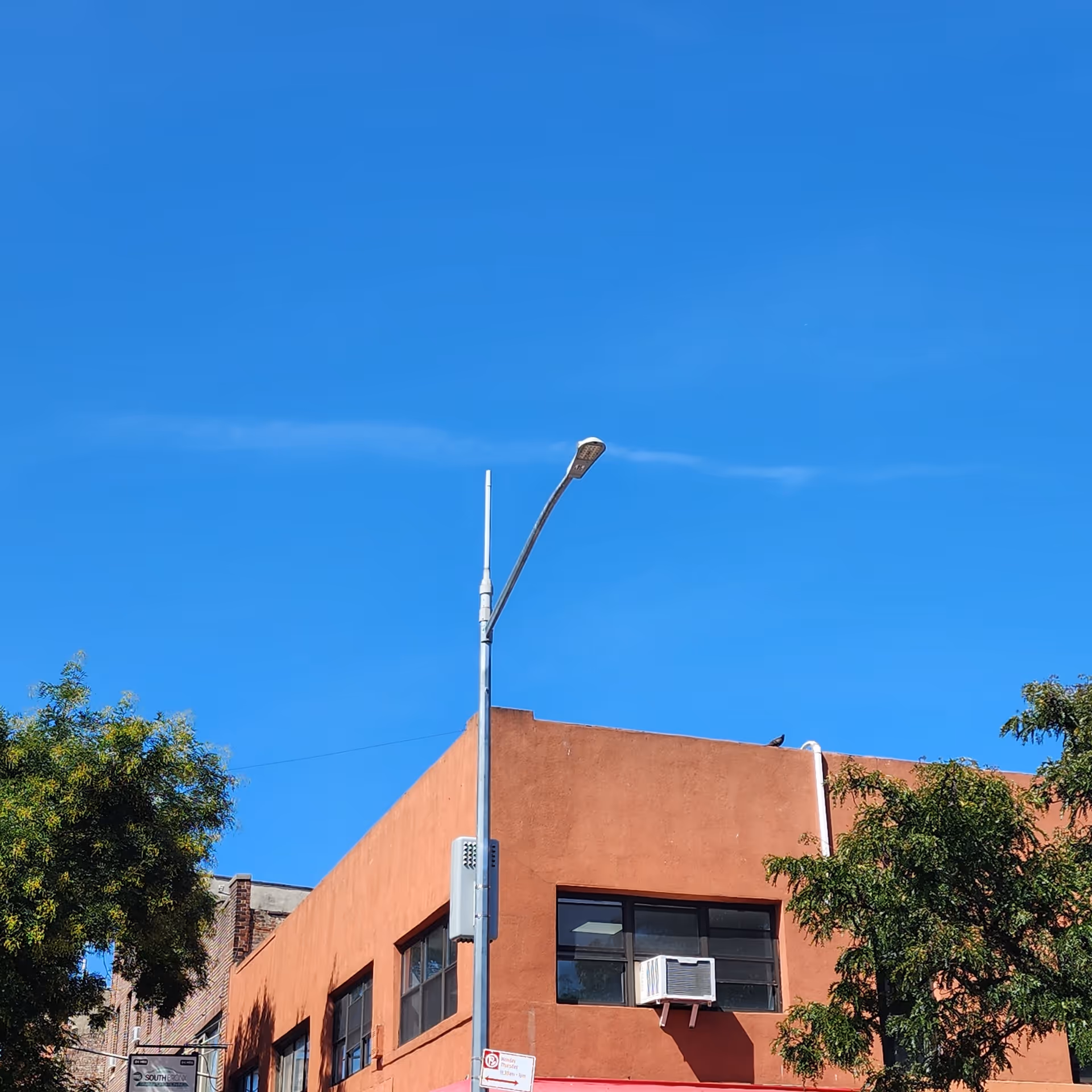 Bright blue sky above an orange building facade with a street lamp and trees.