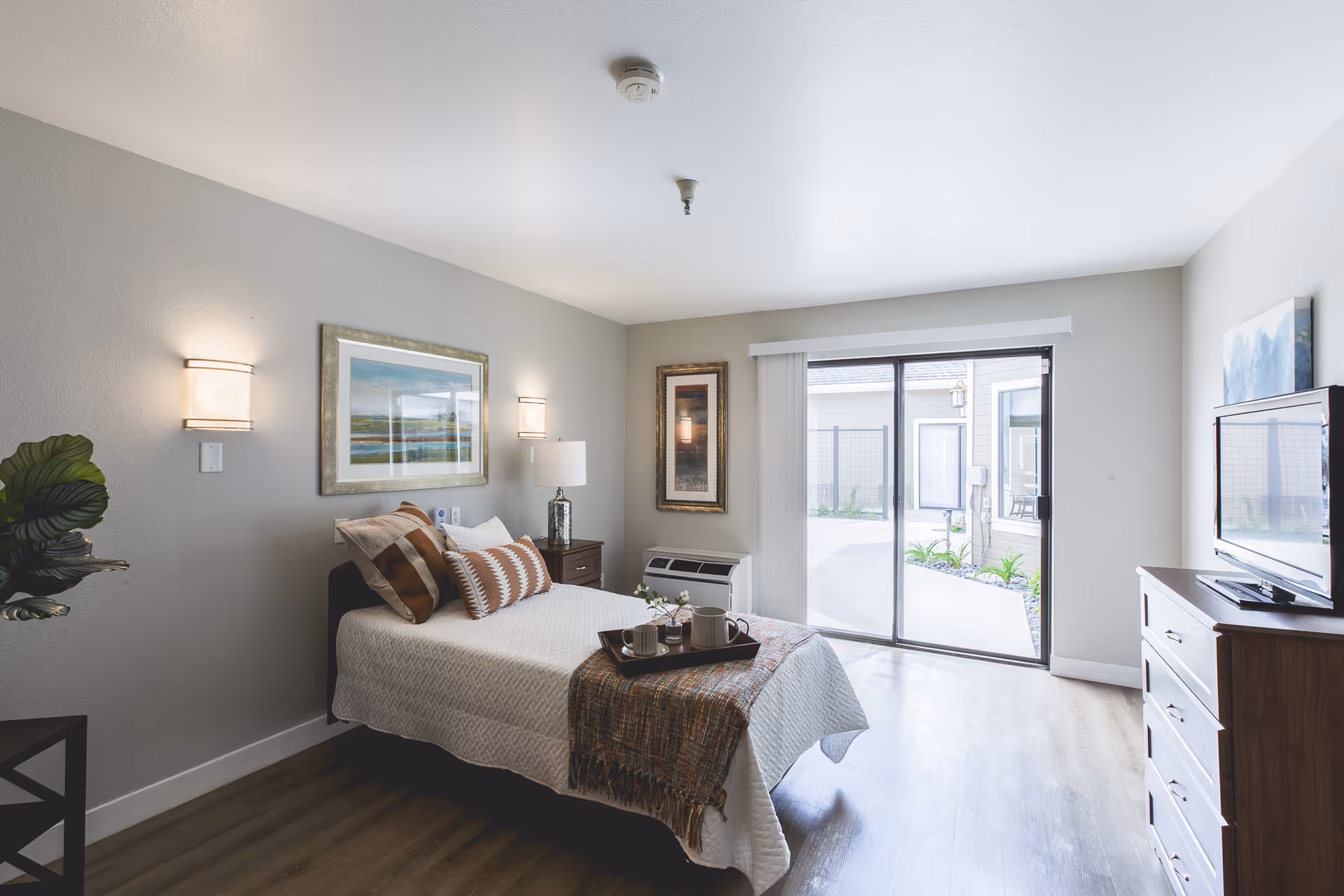 Bright bedroom with a bed, dresser, wall art, and sliding glass door to patio.