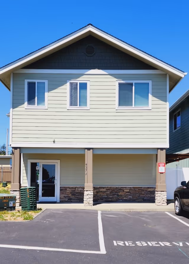 Two-story beige building exterior with stone veneer and front entrance under a gabled roof.
