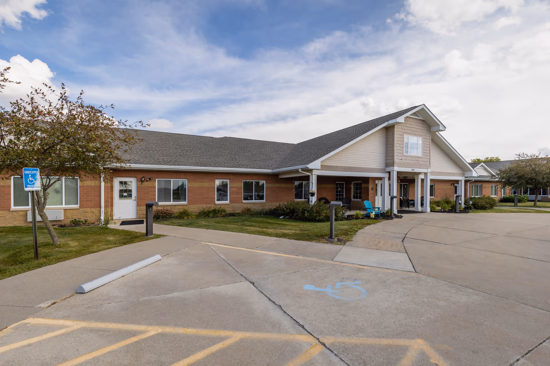Single-story senior living facility building with a covered entrance, driveway, and marked handicap parking space.
