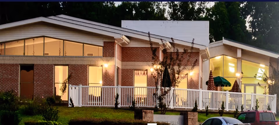 Exterior of Harbert Hills Nursing Home with a lit porch and white railing.