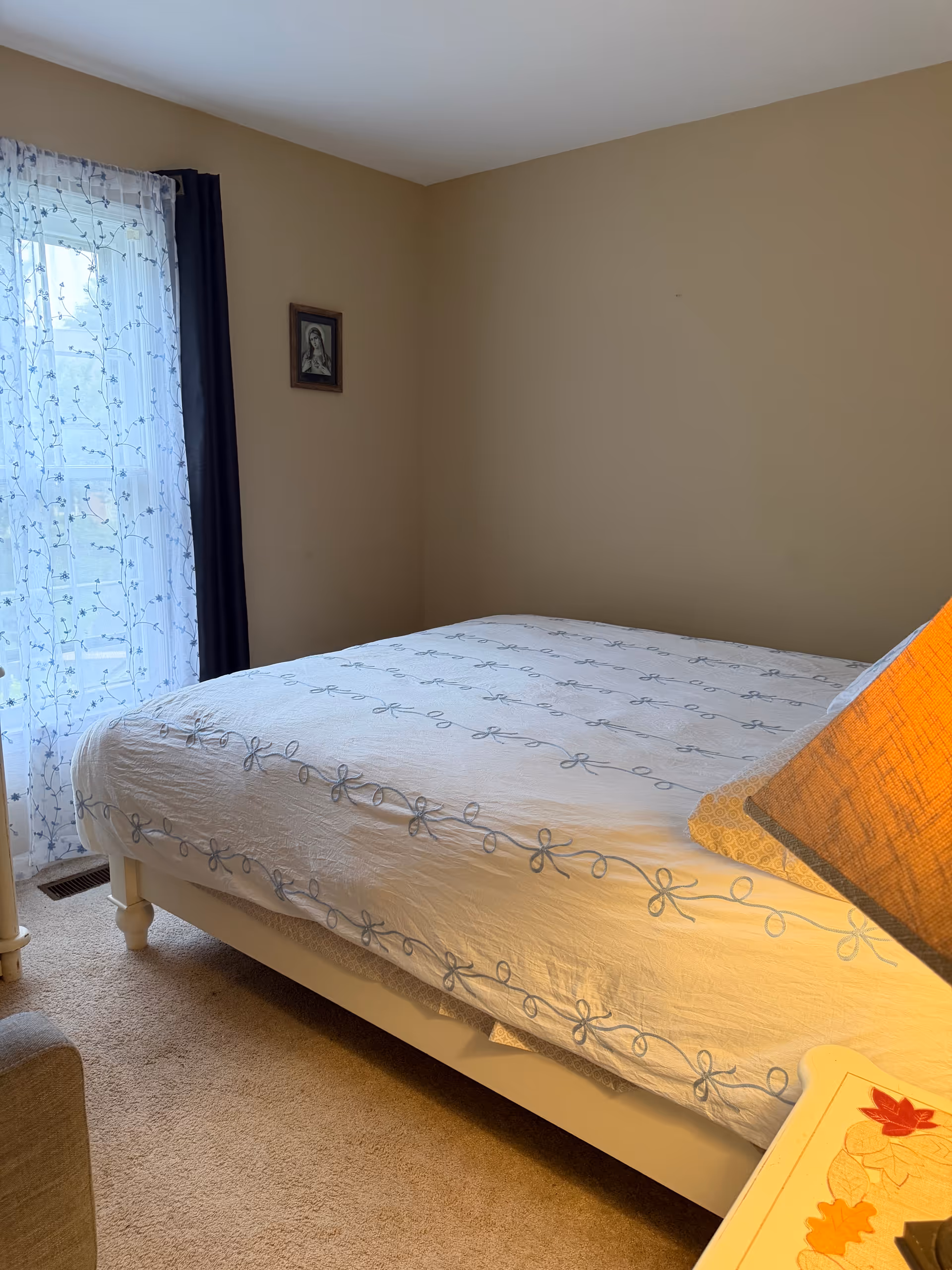 A neatly made bedroom with a bed, sheer curtains, and a bedside table.