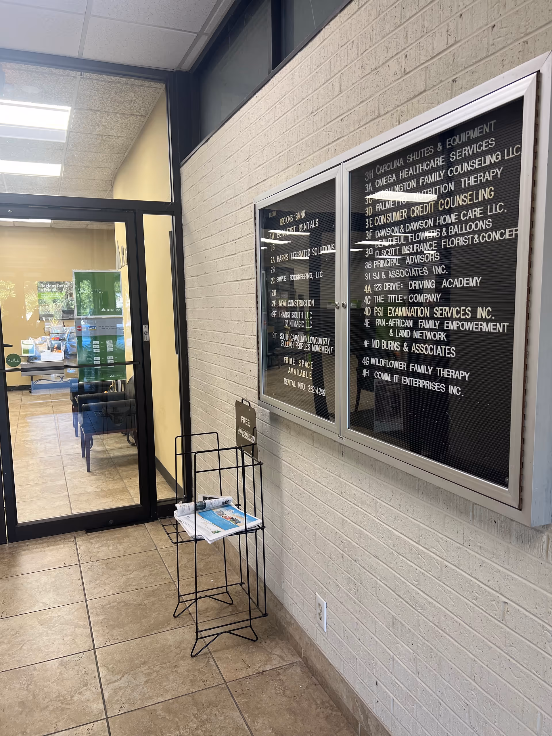 Interior lobby with glass door, brick wall, magazine rack, and large directory board.