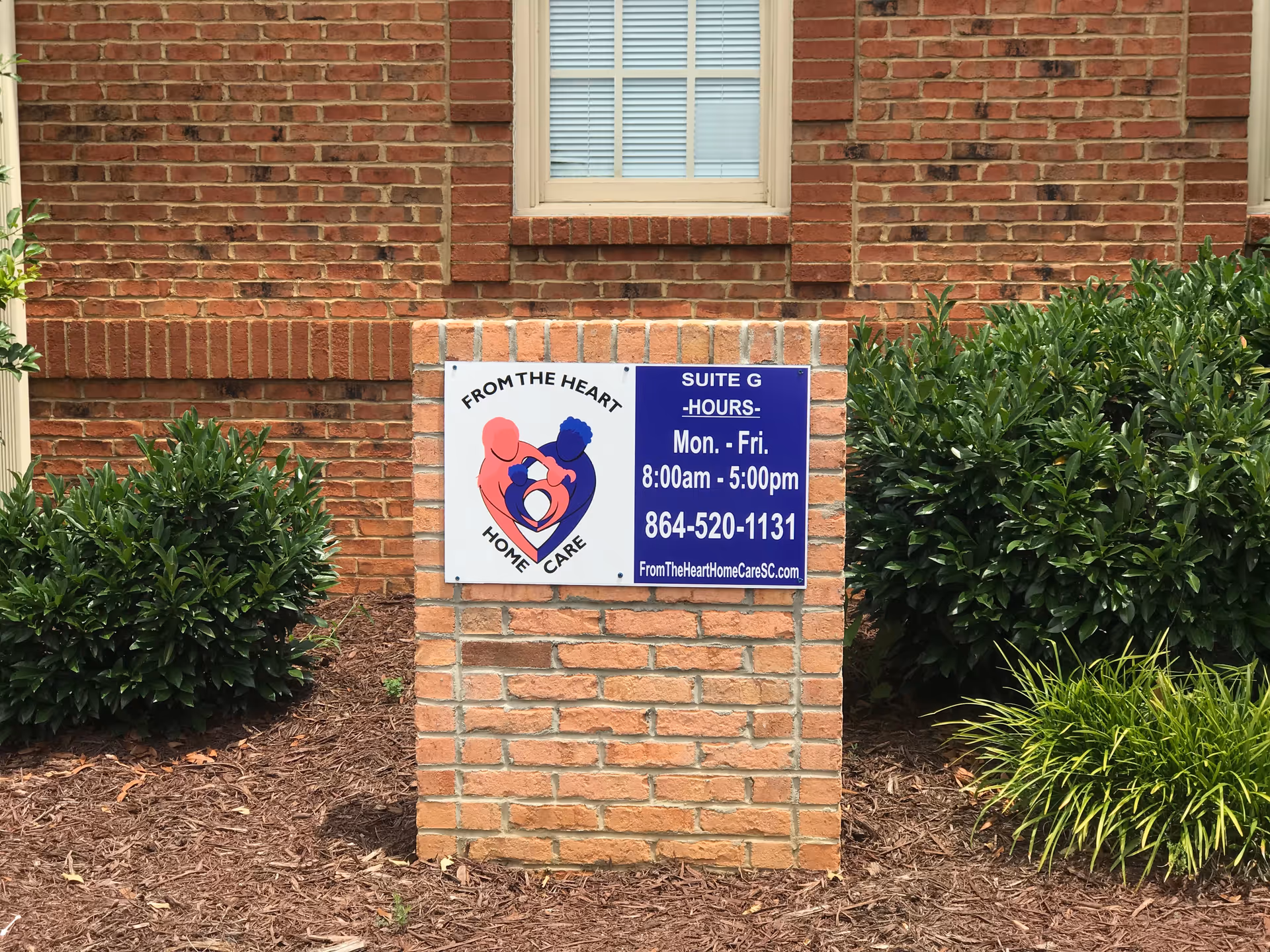 Brick building exterior with a From the Heart Home Care sign and surrounding shrubs.