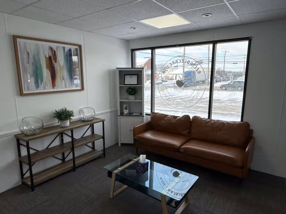 A cozy waiting area with a brown sofa, glass coffee table, and decorative shelves.