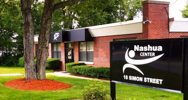 Exterior view of Nashua Center building with a black sign and manicured lawn.