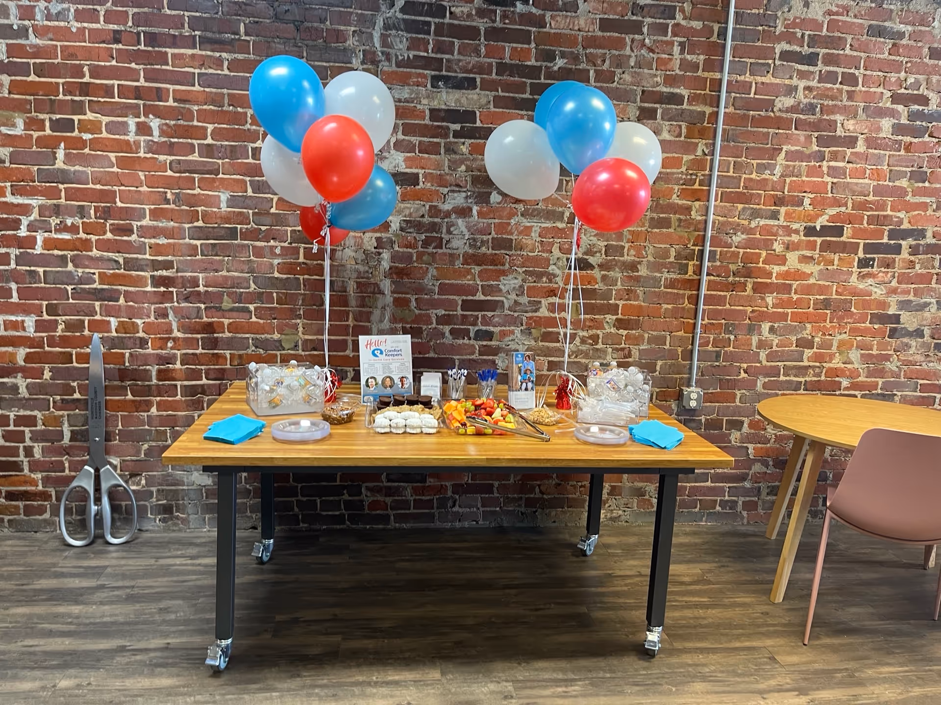 Indoor event table with balloons and snacks against a brick wall in a community space.
