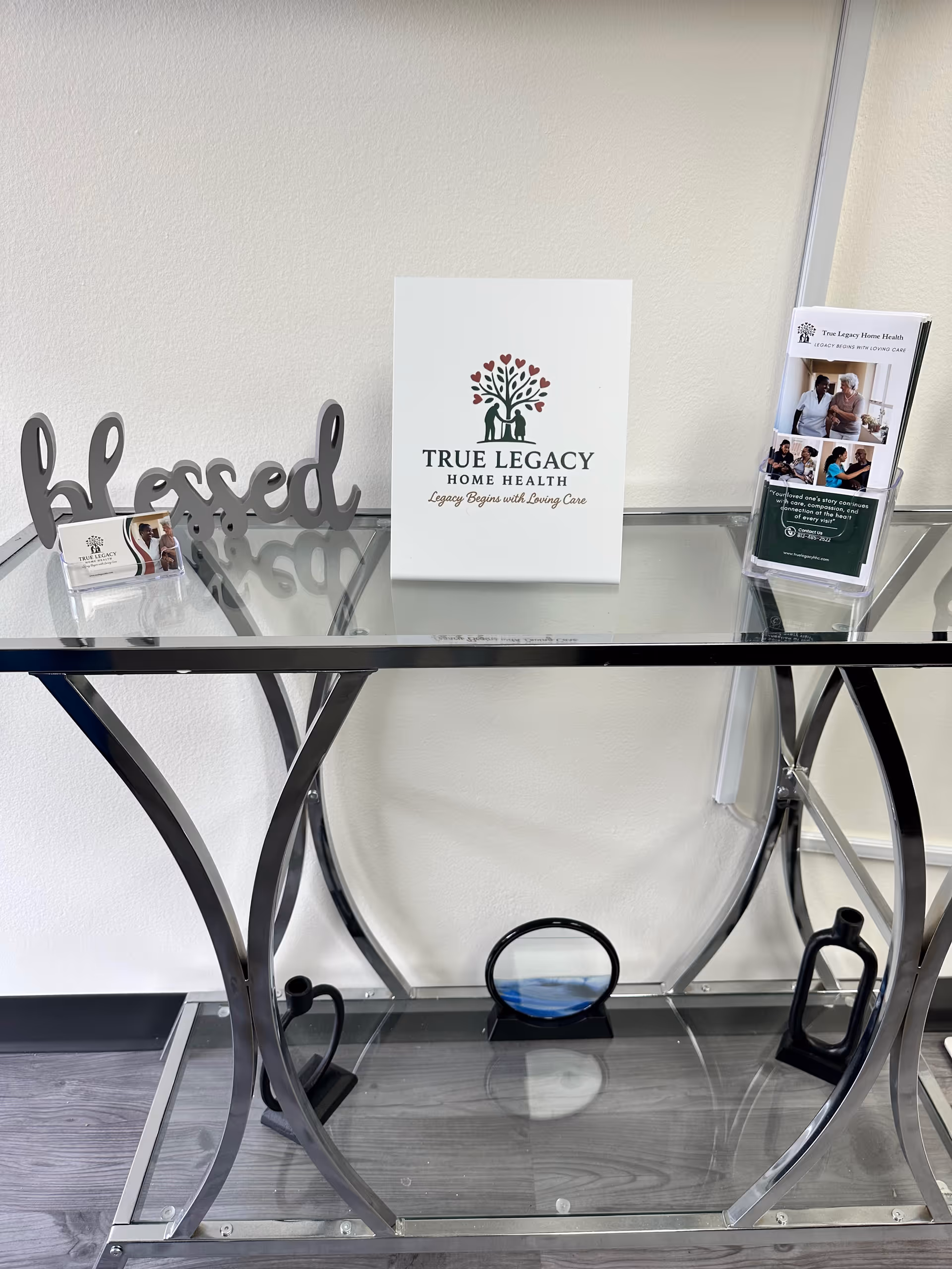 Glass console table with True Legacy Home Health brochure and decorative 'blessed' sign in lobby.