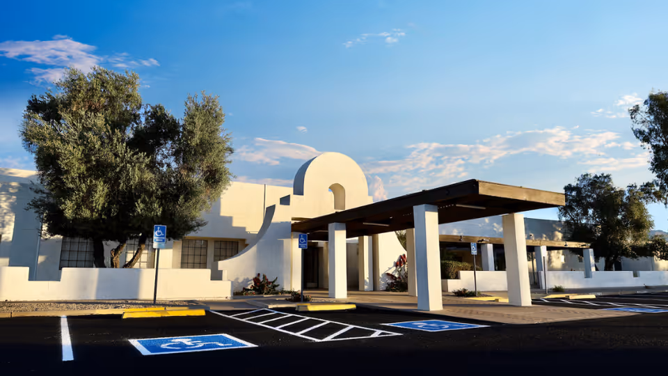 White stucco building with an arched entrance and handicap parking in front.