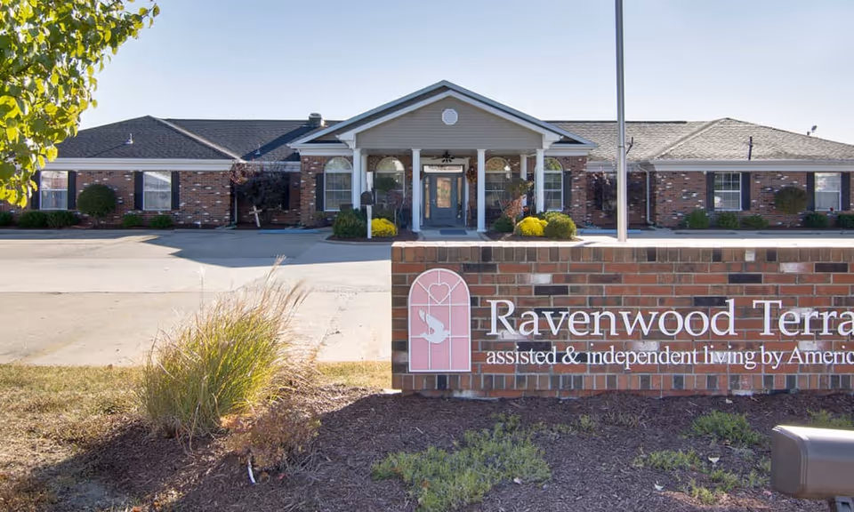 Front exterior of Ravenwood Terrace assisted and independent living facility with a brick entrance sign and covered portico.