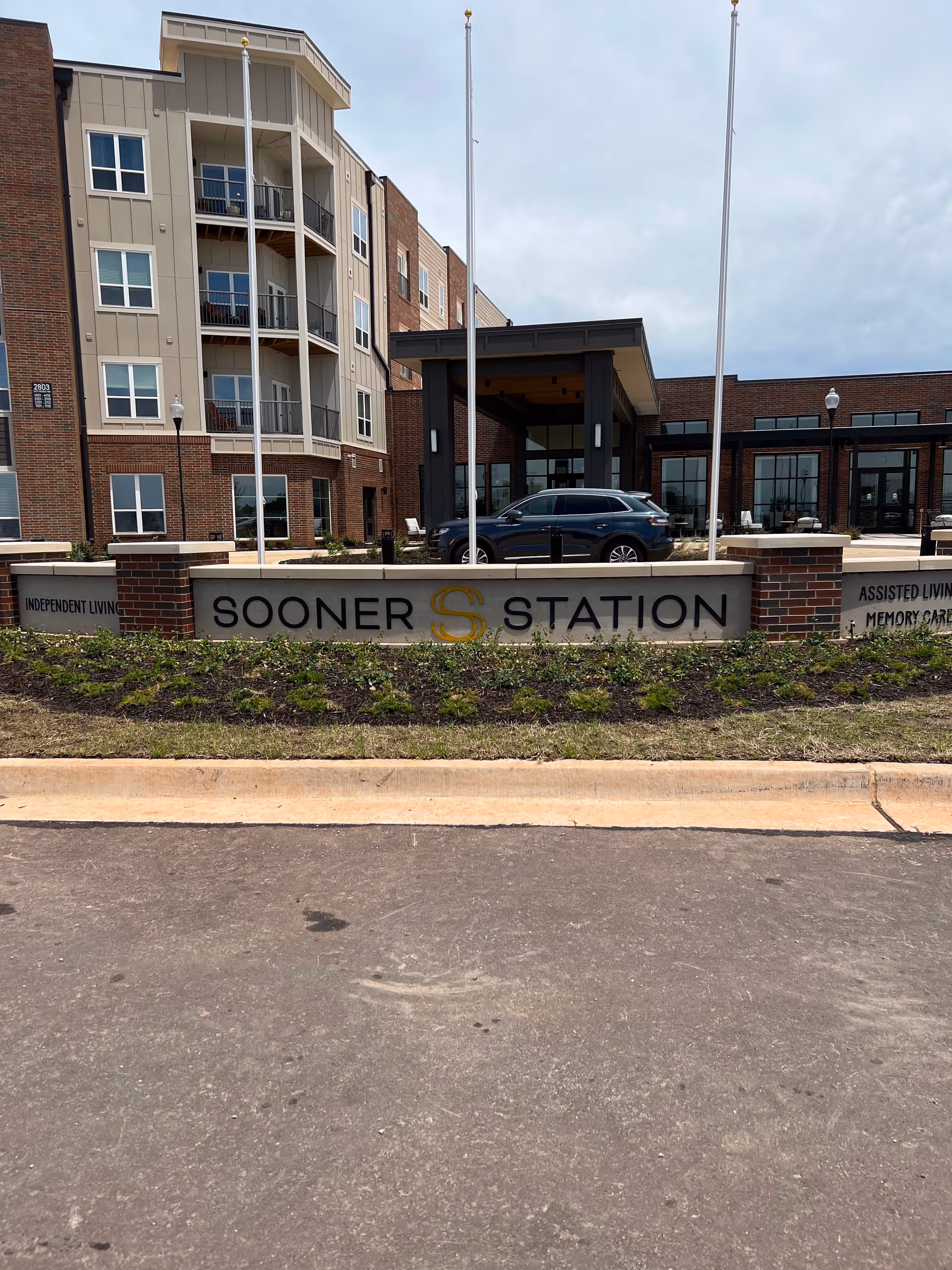 Exterior view of Sooner Station Senior Living entrance with sign and parked cars.
