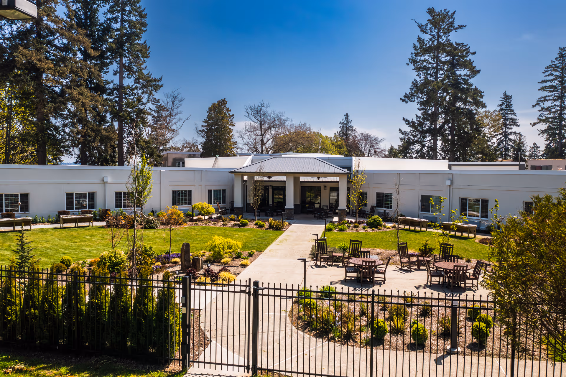 A white, single-story senior living facility with a landscaped outdoor courtyard and patio seating.
