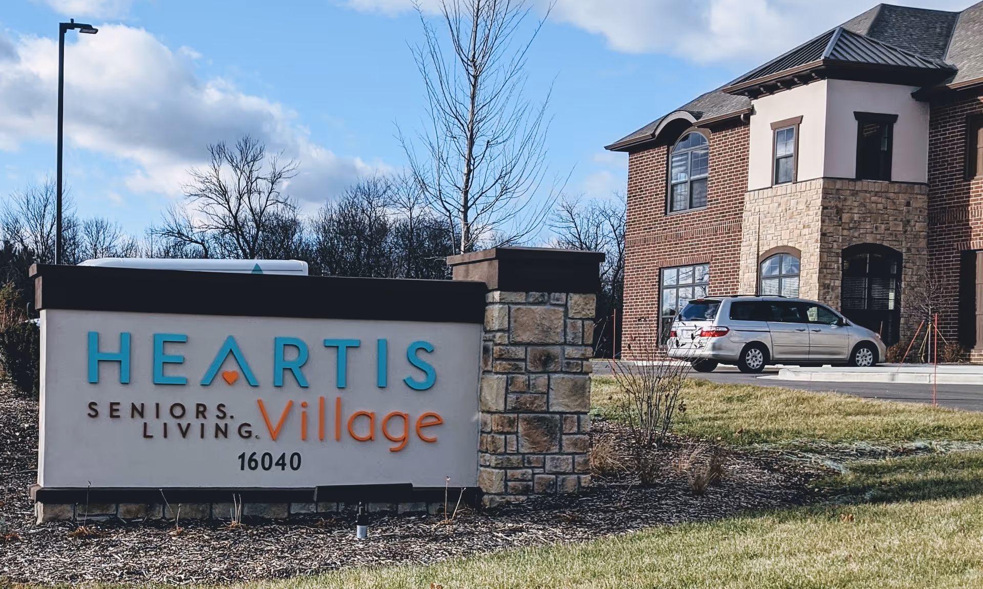 Exterior view of a senior living facility with a large sign and parked minivan.