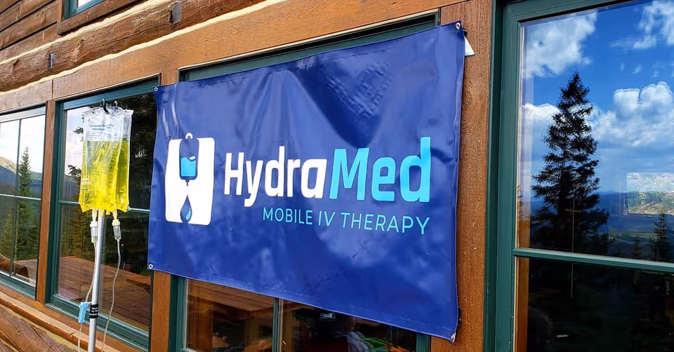 Blue HydraMed Mobile IV Therapy banner hangs on a wooden building exterior with windows.