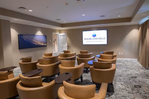 Small screening/media room with rows of tan leather armchairs facing a wall-mounted screen showing the Woodland Hills logo.