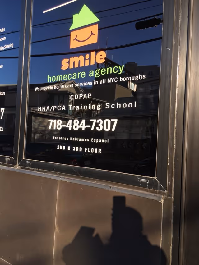 Front window sign for Smile Homecare Agency with contact number and bilingual note.