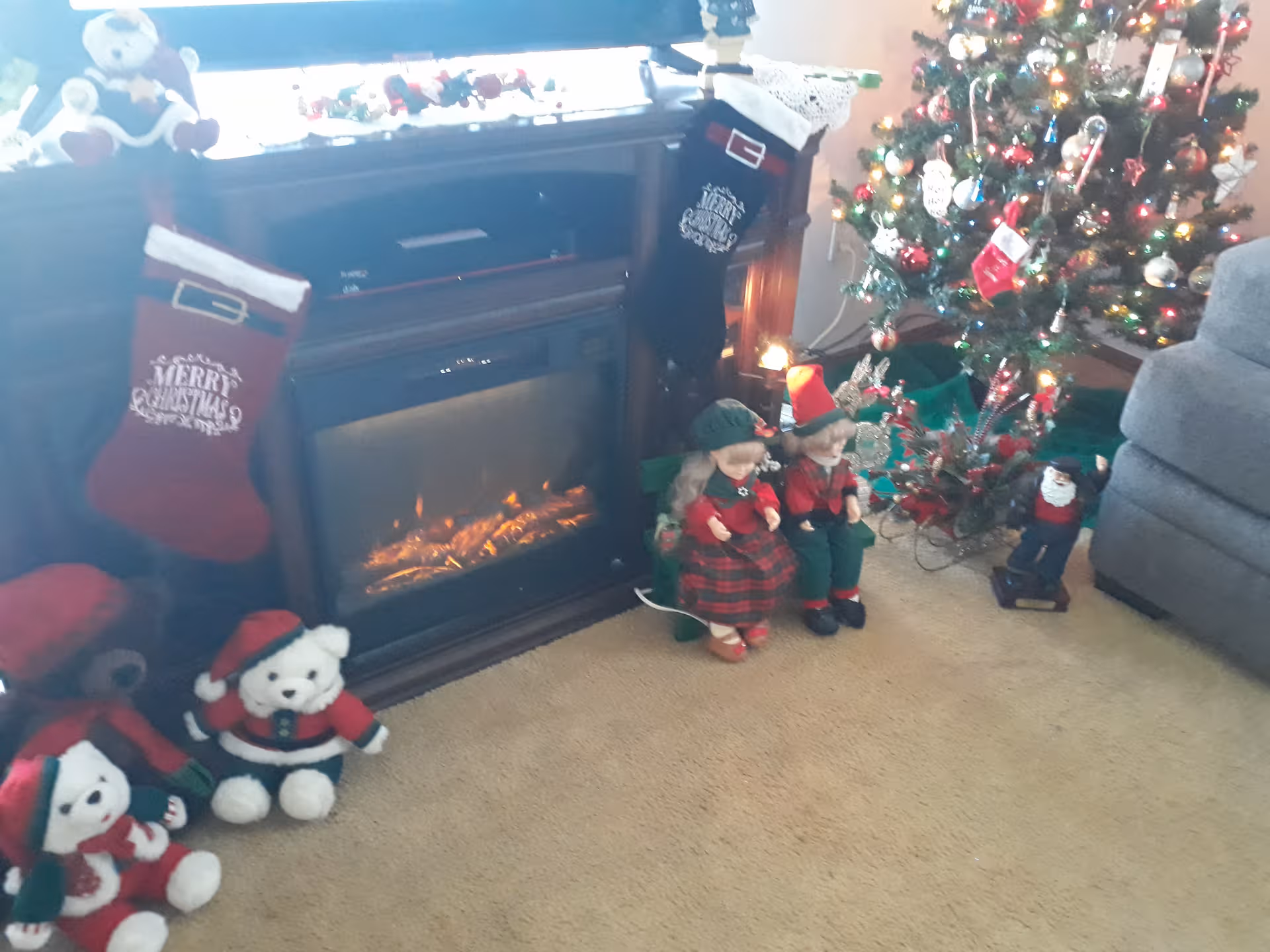 Cozy living room with Christmas tree, fireplace, stockings, and festive decorations.