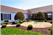 An outdoor courtyard with circular stone patio, trimmed bushes, and a single-story care center facade.
