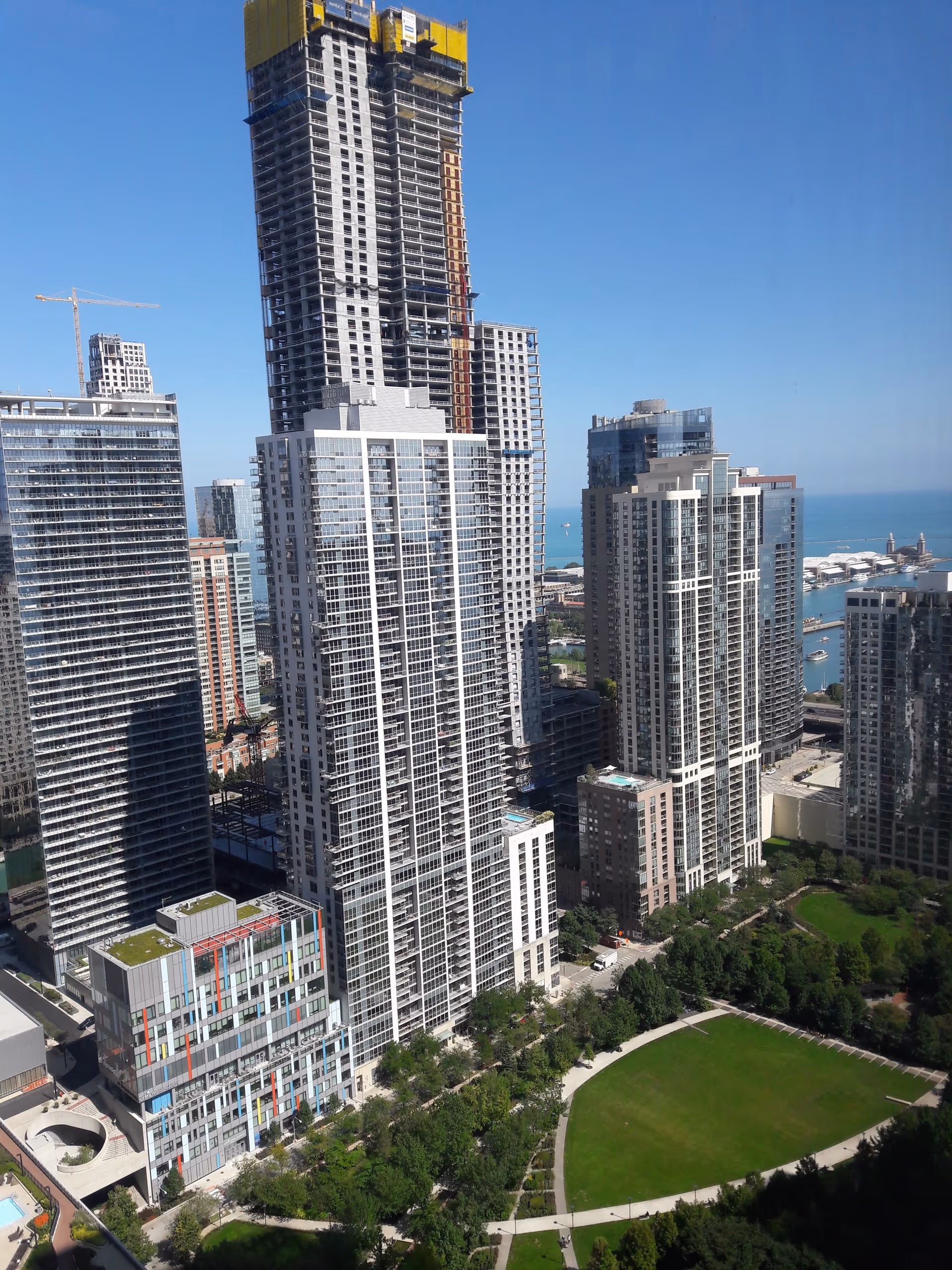Tall skyscrapers dominate a city waterfront with a green park in the foreground.