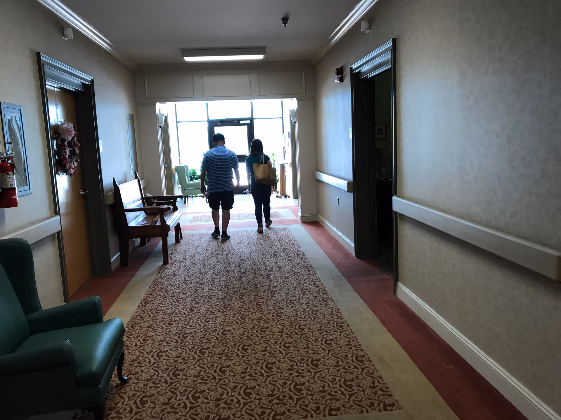 Interior hallway of a senior living facility with two residents walking toward the daylight.