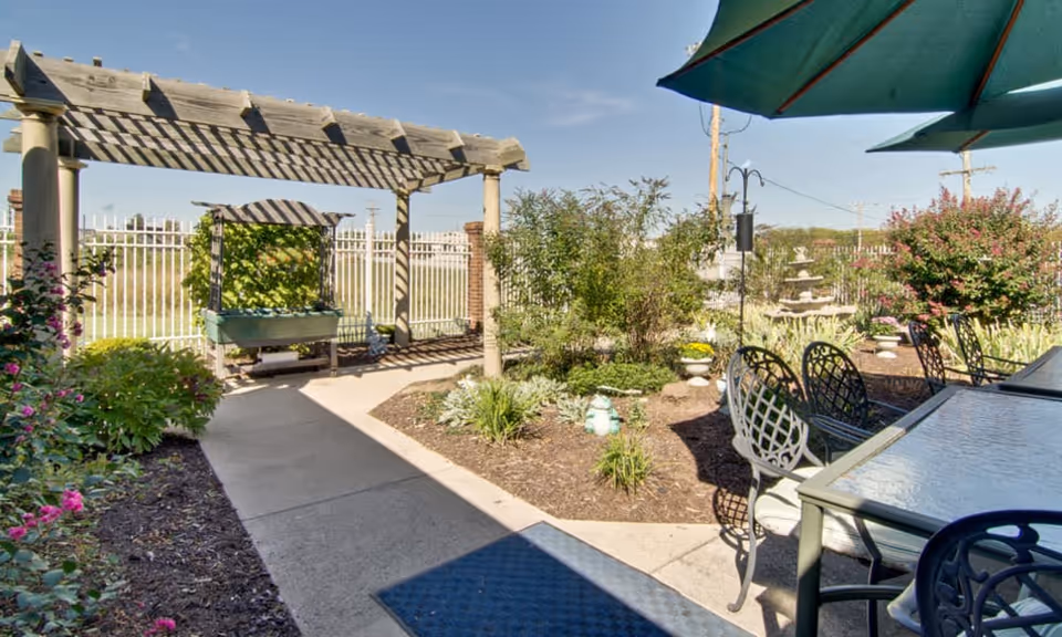 Outdoor courtyard with a wooden pergola, paved walkway, planted garden beds, patio tables and umbrellas.