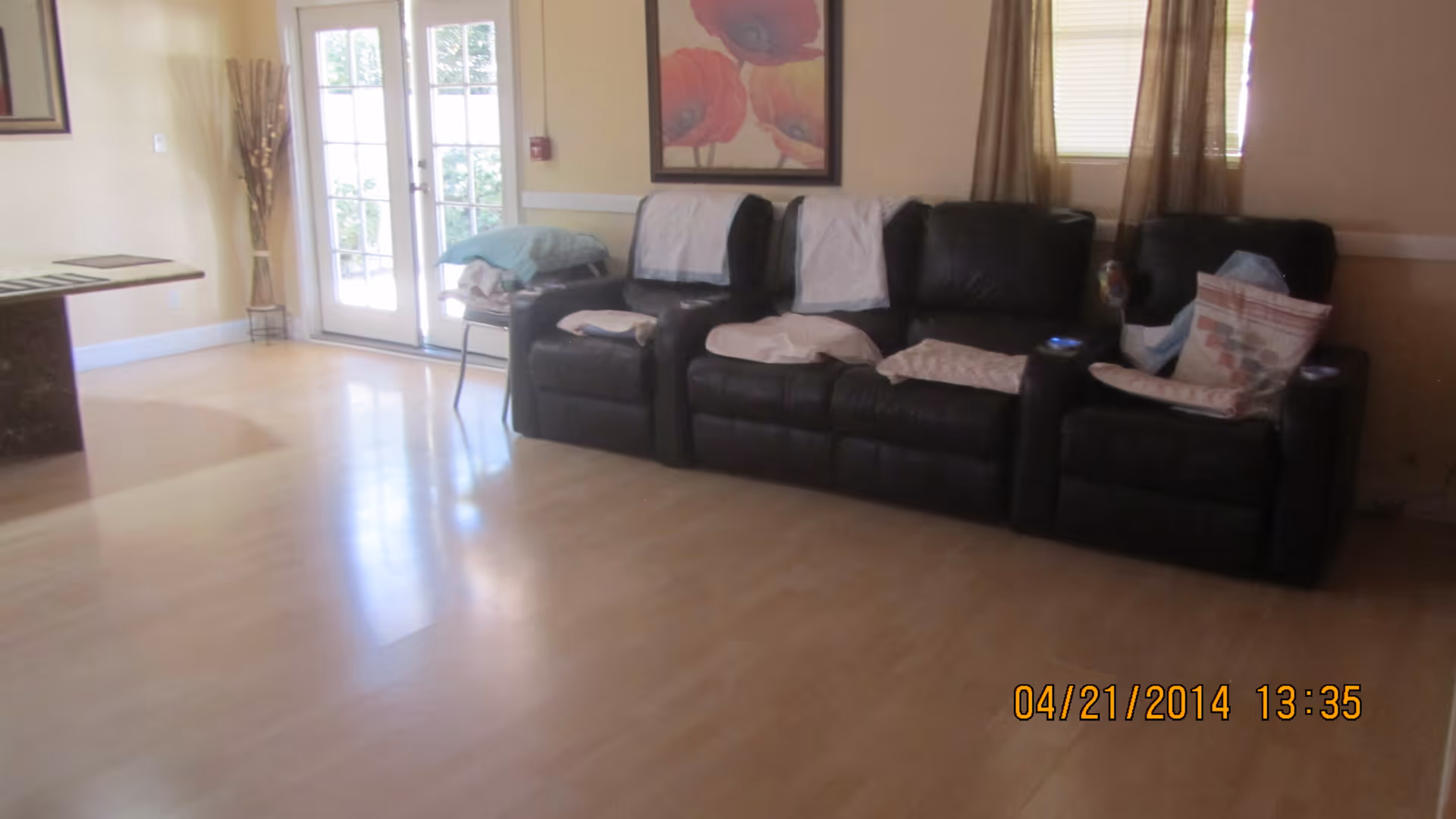 Sunlit living room with three black leather recliners along a wall, hardwood floors and French doors.