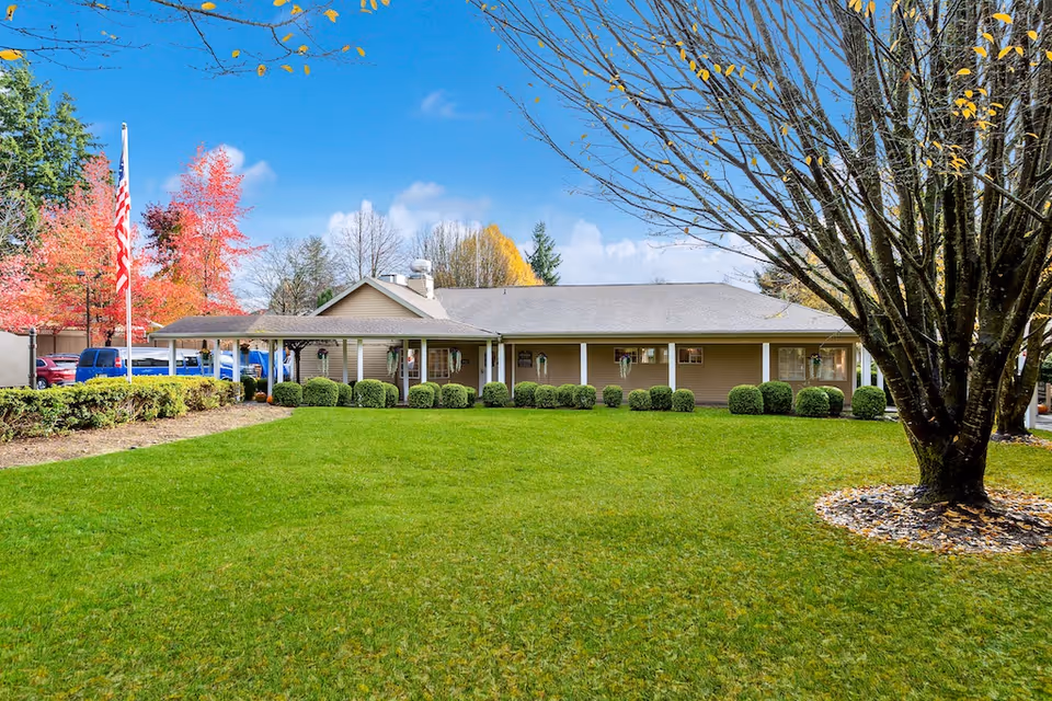 Single-story building with a wide green lawn, shrubs, an American flag, and a large tree in front.