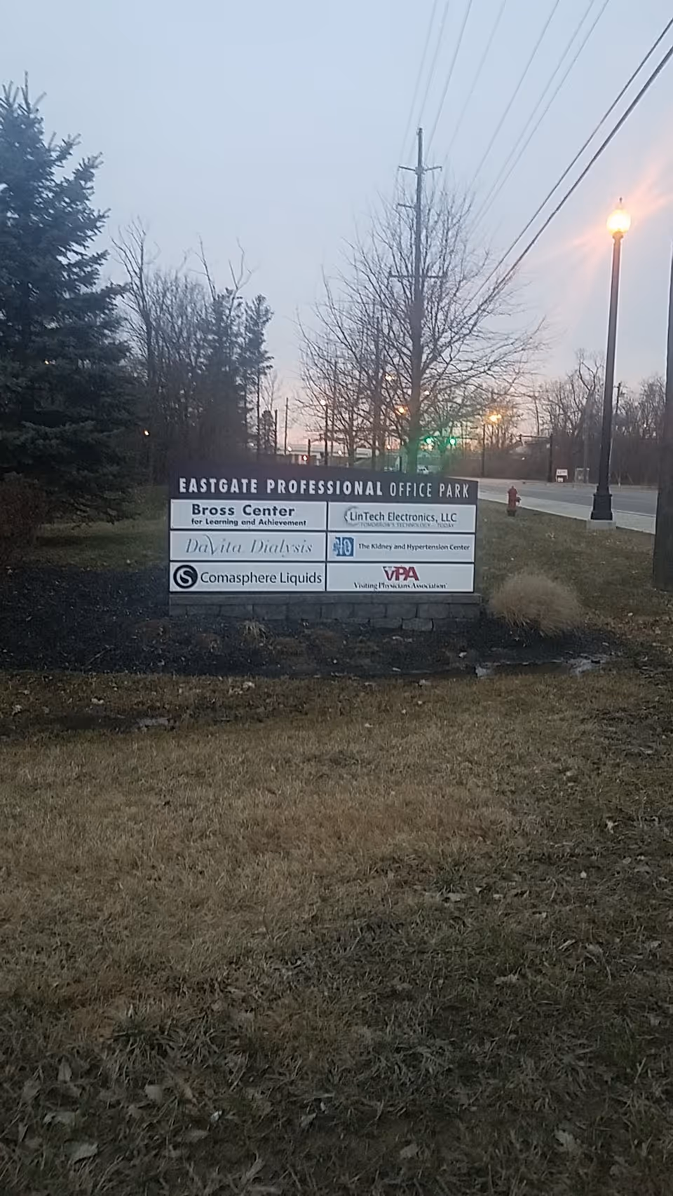 Outdoor sign for Eastgate Professional Office Park with trees, streetlights, and a roadway.