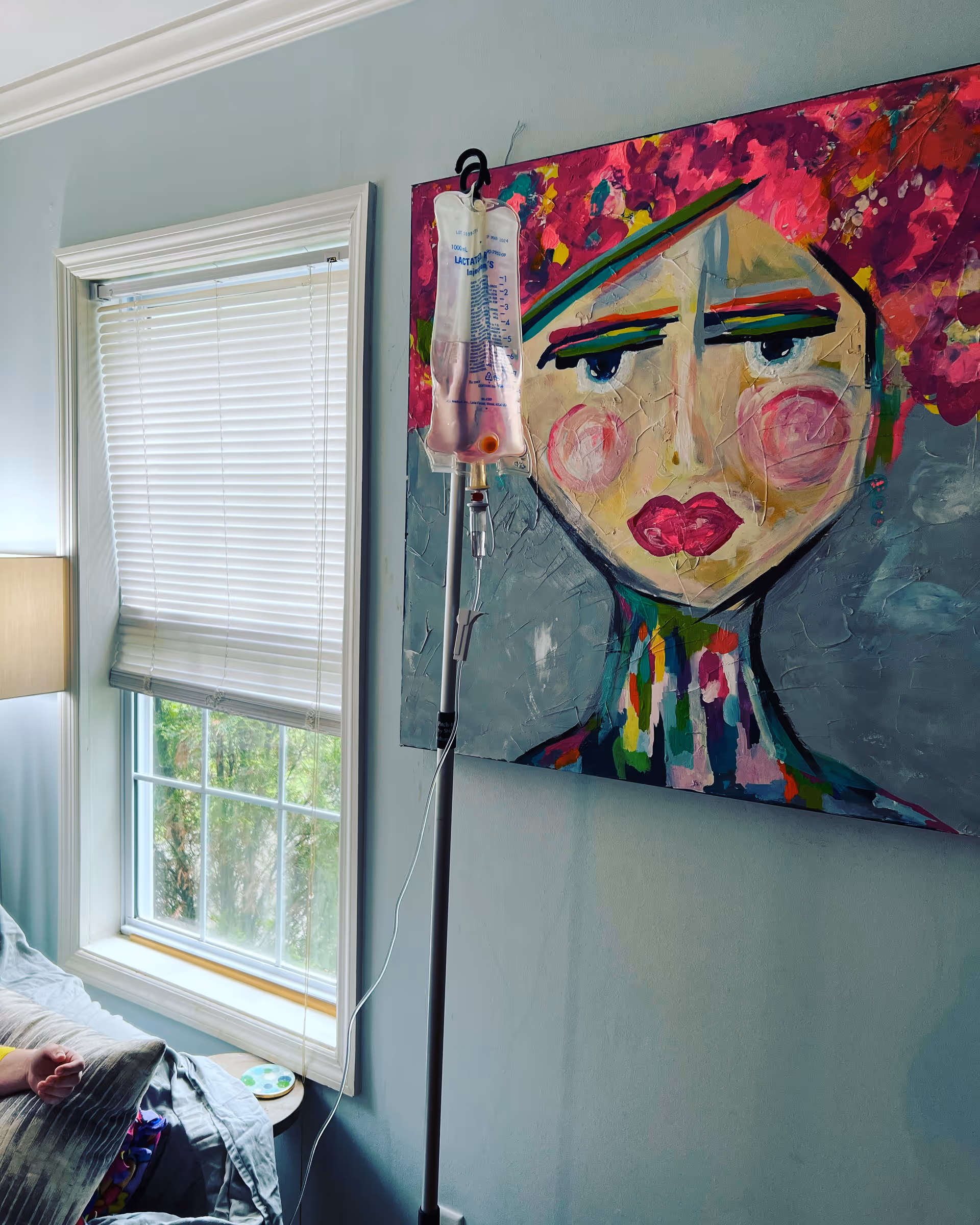IV pole with bag beside a colorful portrait in a pale blue room.