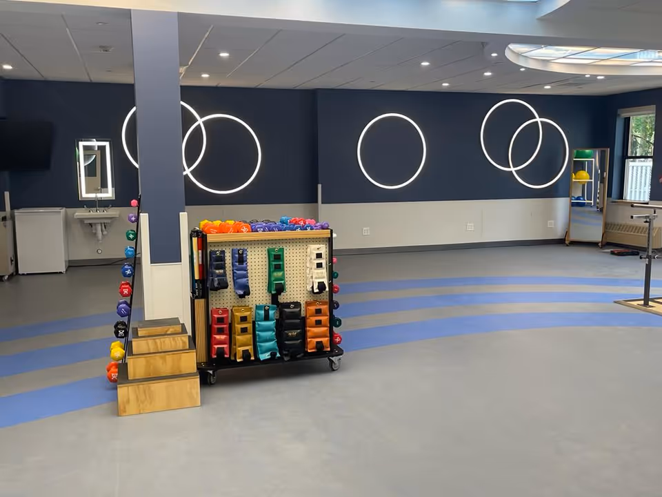 Interior fitness area at Teaneck Nursing Center with weights and circular wall lights.