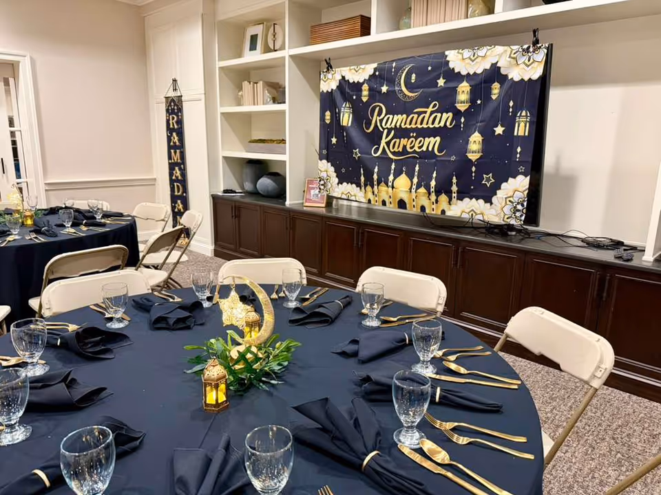 Tables with navy linens and gold flatware in a dining room, Ramadan Kareem banner on screen.