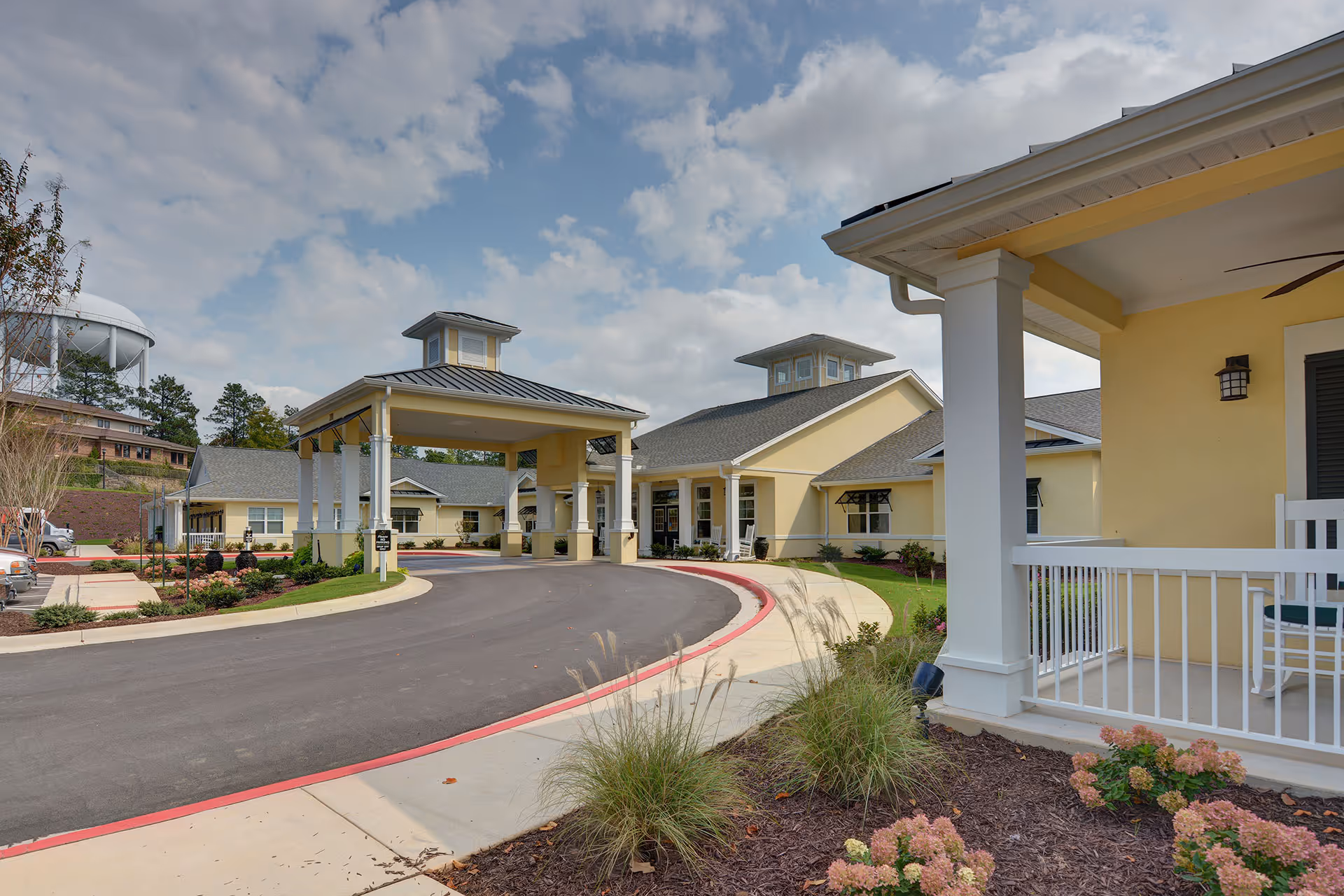 Entrance driveway and covered porte-cochere of a yellow senior living facility building with landscaped grounds and a porch.
