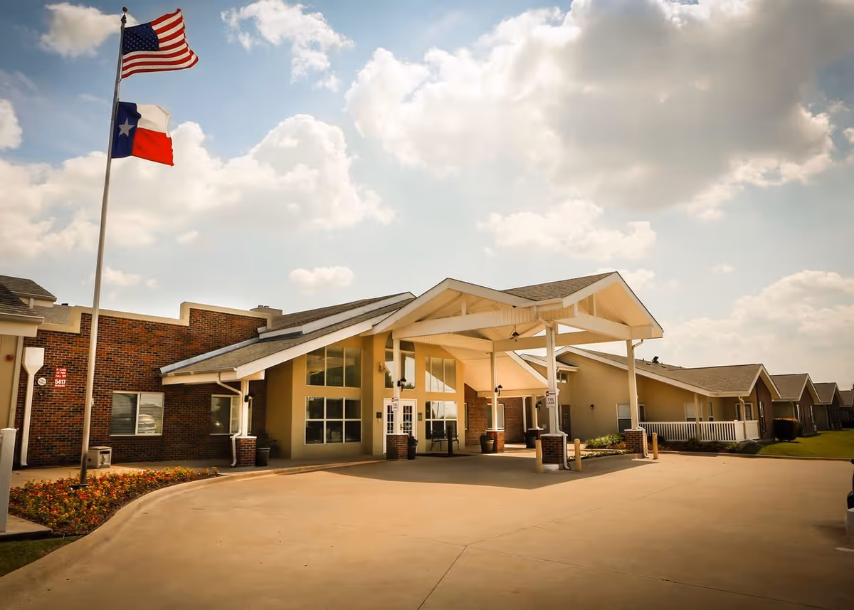 Front view of a senior living facility with a covered entrance and flagpoles.
