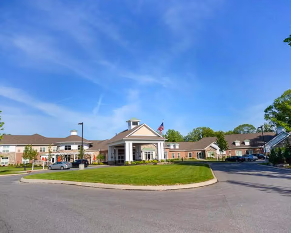 A senior living campus exterior with a circular driveway and central entrance under a clear sky.