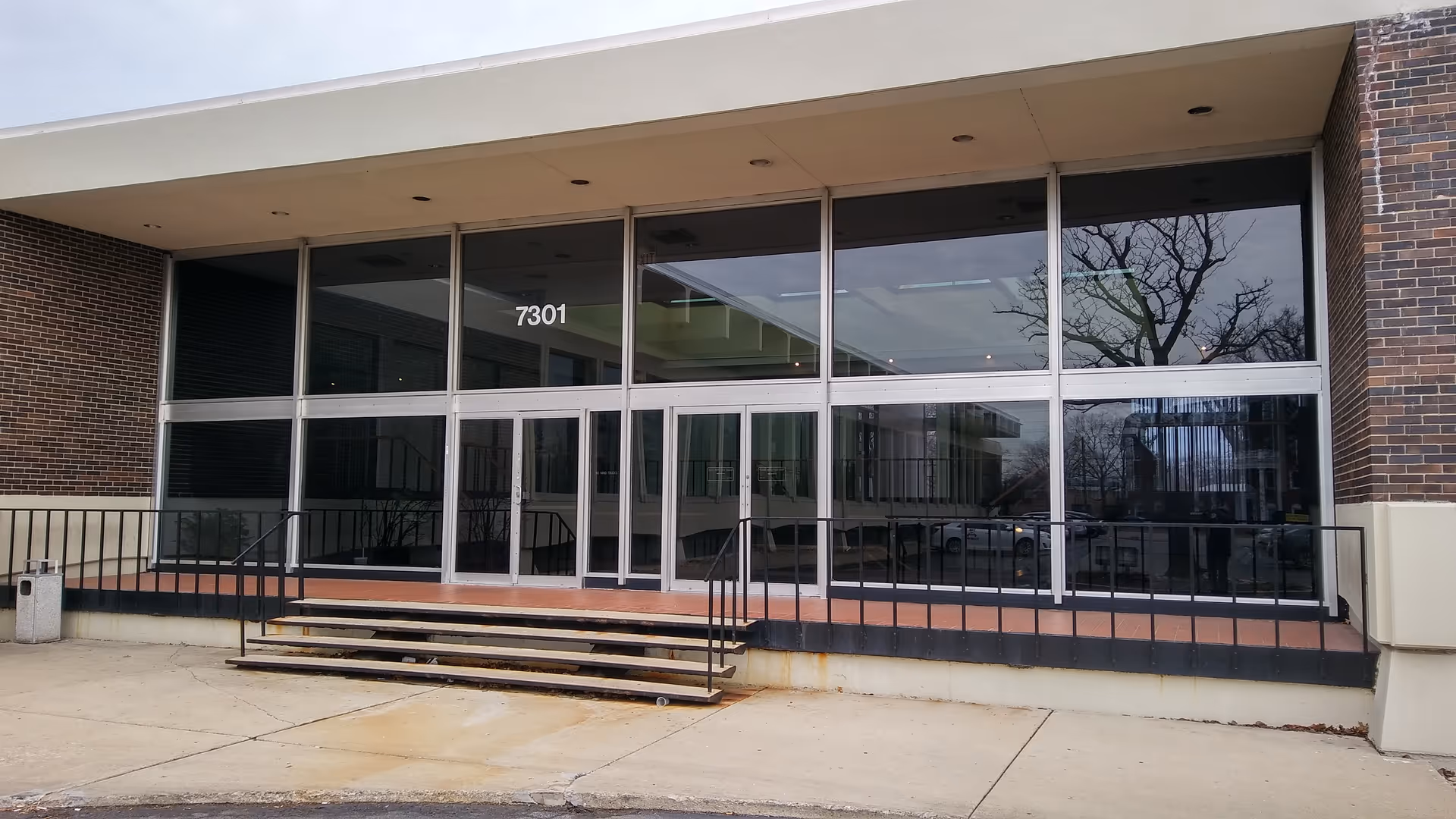 Glass-front entrance of a brick senior living facility with steps and ramp.