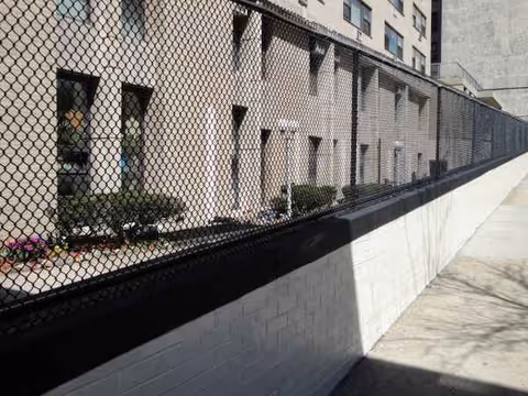 Exterior view of a building with a chain-link fence and sidewalk along a sloped wall.