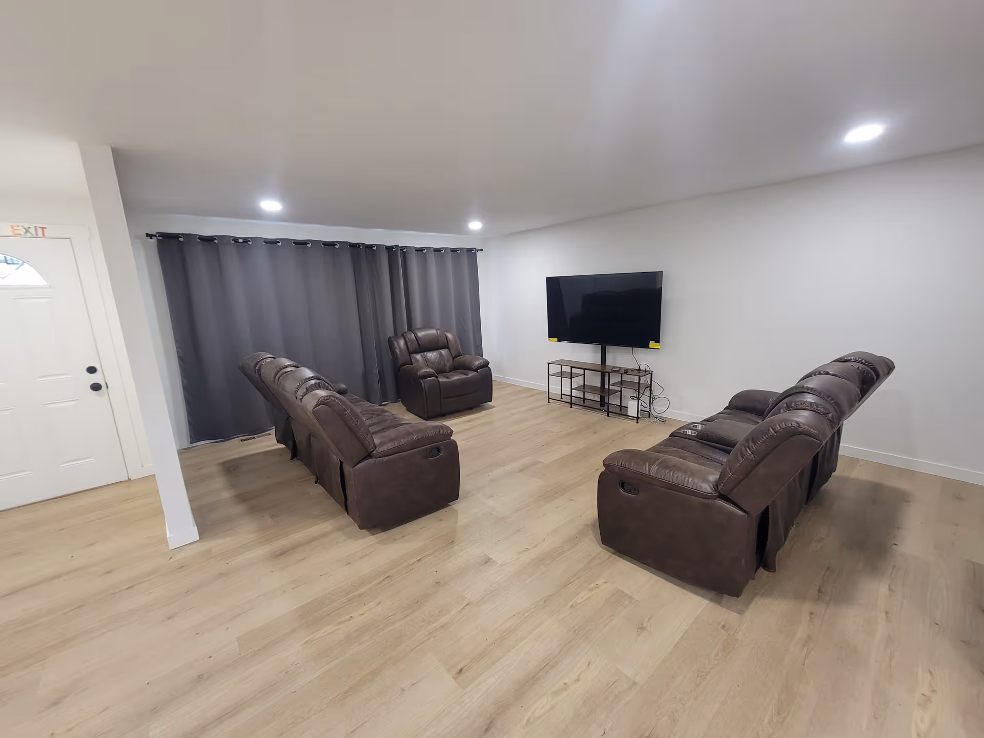 Spacious living room with multiple brown leather recliners and a wall-mounted TV.