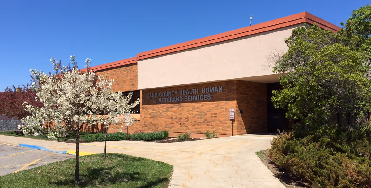 Brick facility with Cass County Health, Human Services sign and blooming trees.