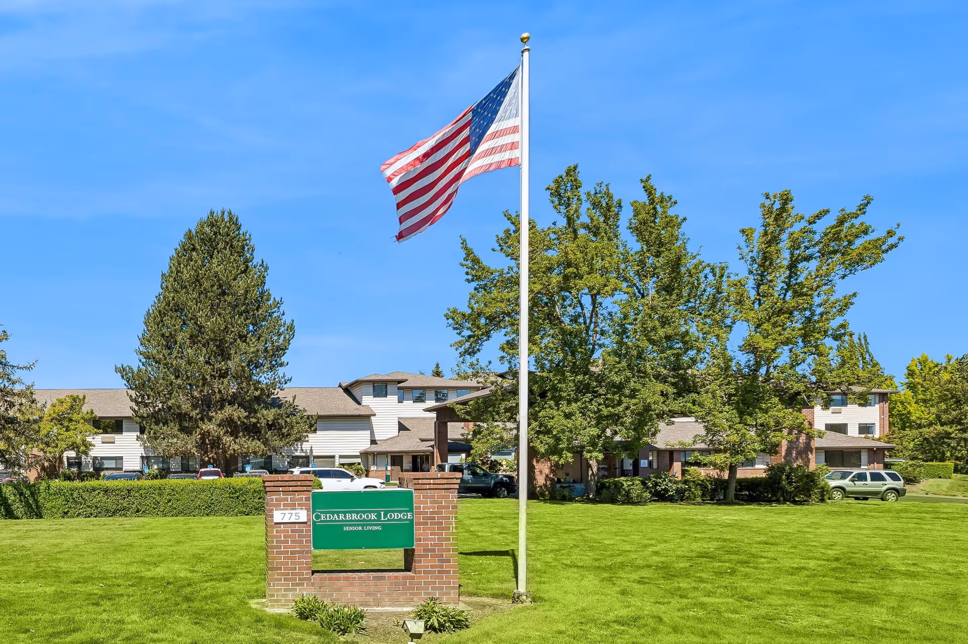 Well-kept lawn, flagpole, and Cedarbrook Lodge Senior Living exterior sign in front.