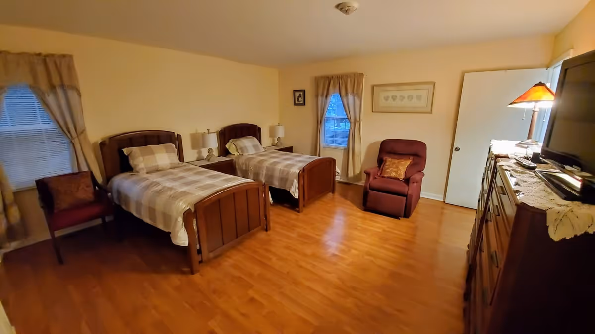 Two twin beds with matching wood headboards, dresser, and recliner in a cozy senior living bedroom.