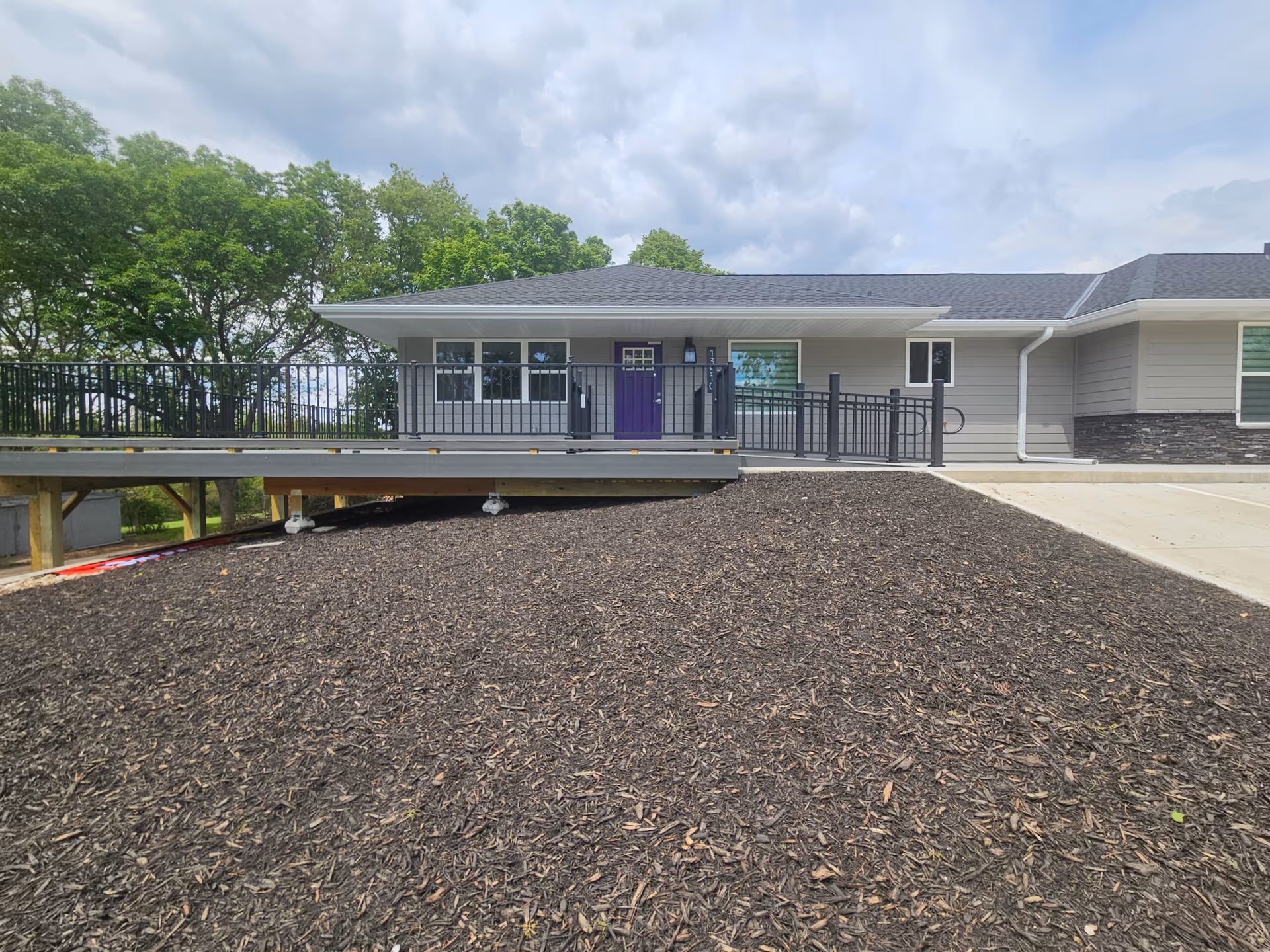Single-story facility exterior with ramp and railing to a purple front door, surrounded by trees.