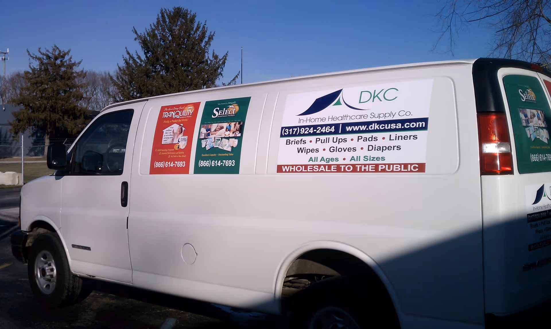 White delivery van with multiple advertisements parked outdoors, featuring Diaper King Club branding.
