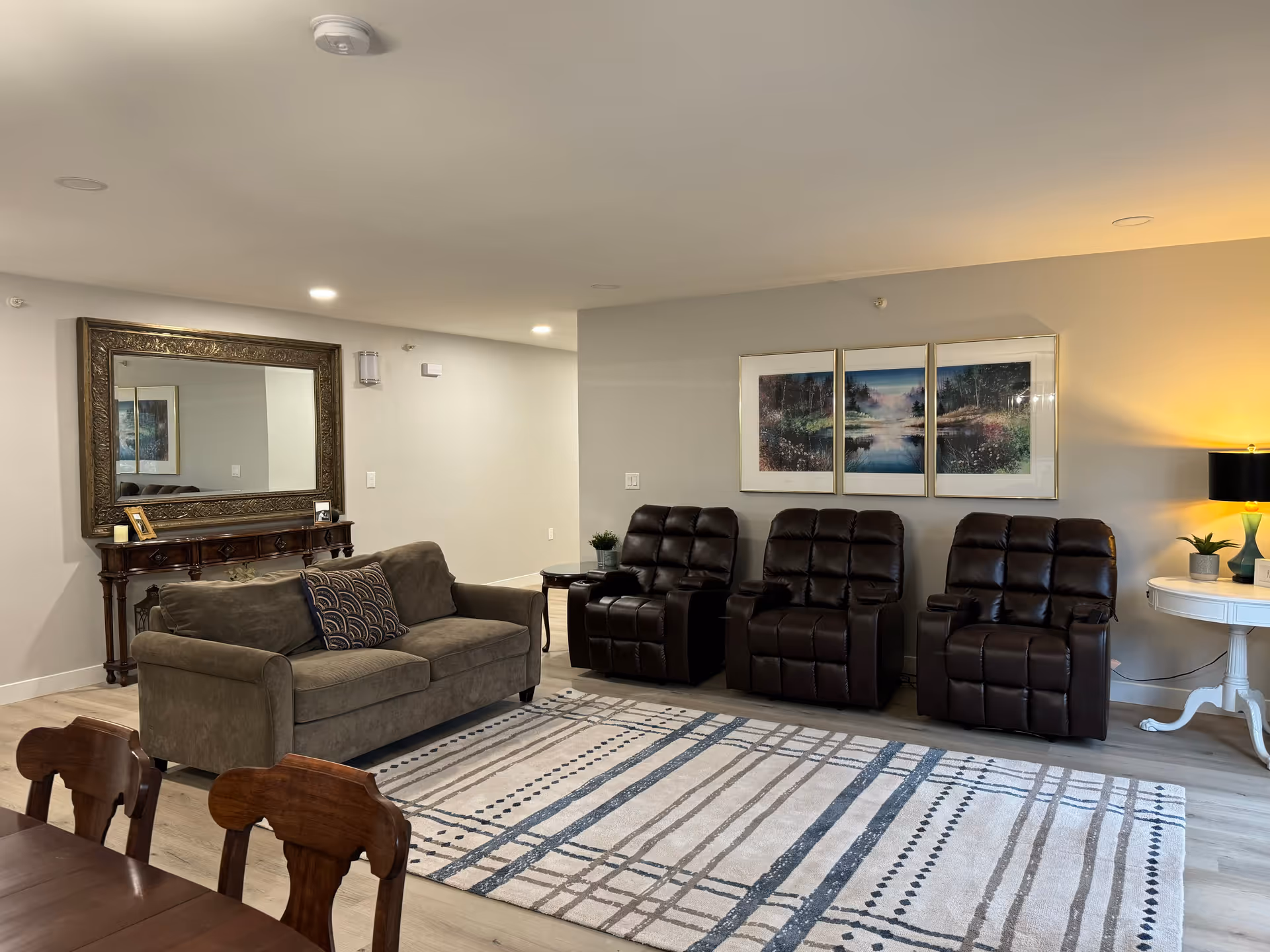 Cozy common living area with sofa, recliners, framed art, and a striped rug.