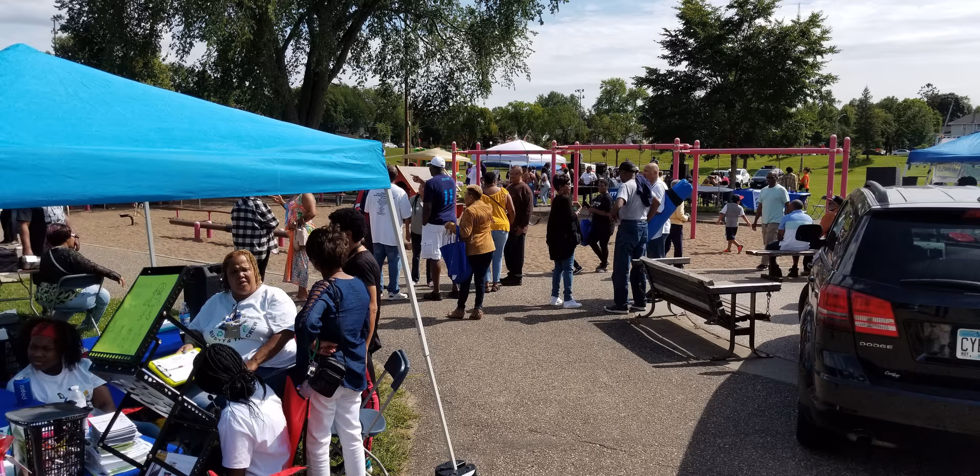 Outdoor community event with tents, people, and a playground in a parking lot.