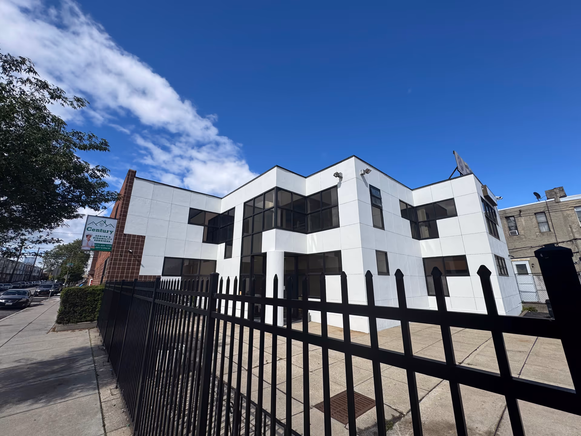 Modern white facility building labeled Century Home Care LLC, with black fence and blue sky.